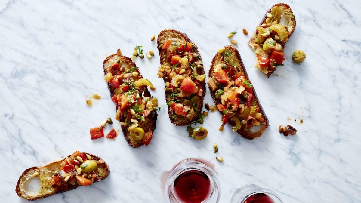 Vier Scheiben gebackenes Ciabatta-Brot belegt mit gegrilltem Gemüse,: Tomaten, Paprika, Oliven und Sellerie, dazu Pinienkerne